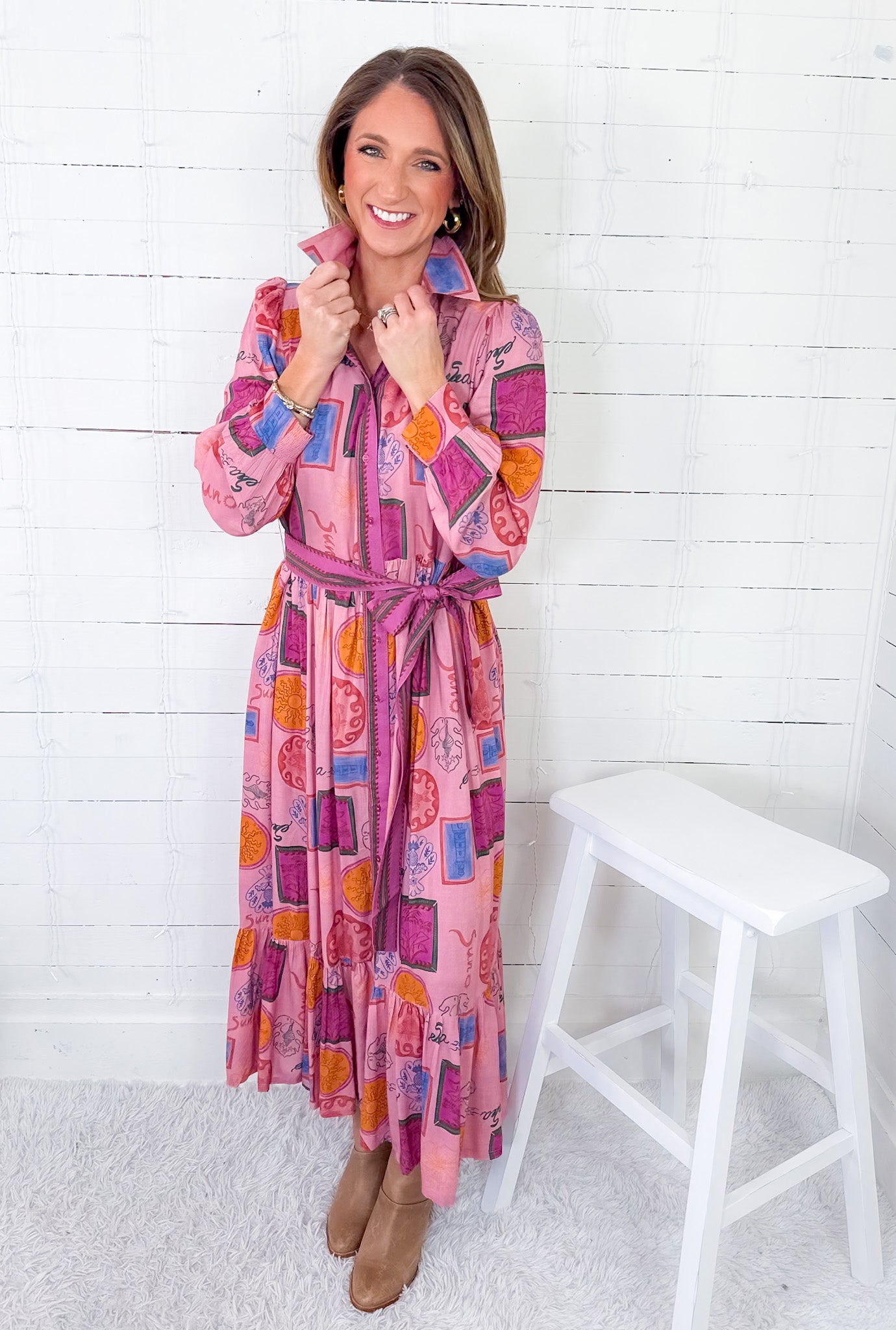 Woman wearing a colorful patterned dress standing against a white wooden panel background