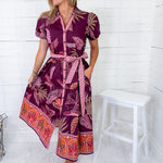 Woman wearing a patterned dress standing against a white wooden panel background