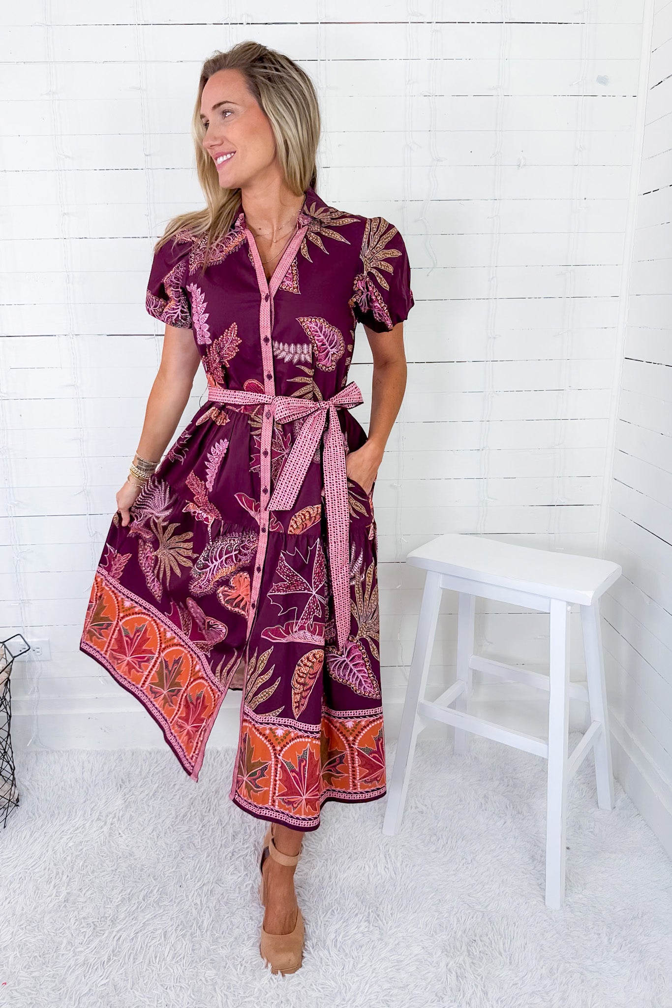 Woman wearing a patterned dress standing against a white wooden panel background