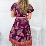 Woman wearing a purple patterned dress sitting on a white chair against a white wooden panel background