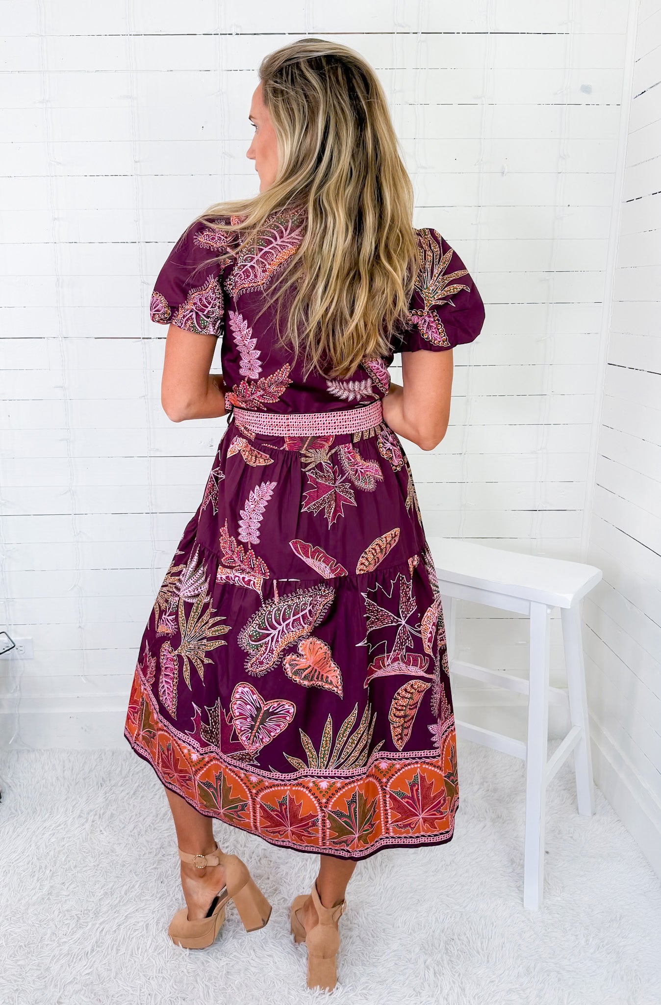 Woman wearing a purple patterned dress sitting on a white chair against a white wooden panel background