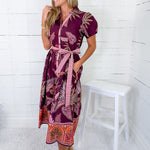 Woman wearing a patterned dress standing in a room with white walls and a white stool.