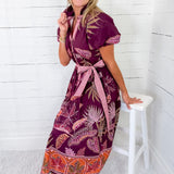Woman wearing a patterned dress sitting on a white stool against a white wooden paneled wall.