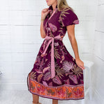 Woman wearing a patterned dress sitting on a white stool against a white wooden panel background