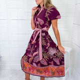 Woman wearing a patterned dress sitting on a white stool against a white wooden panel background