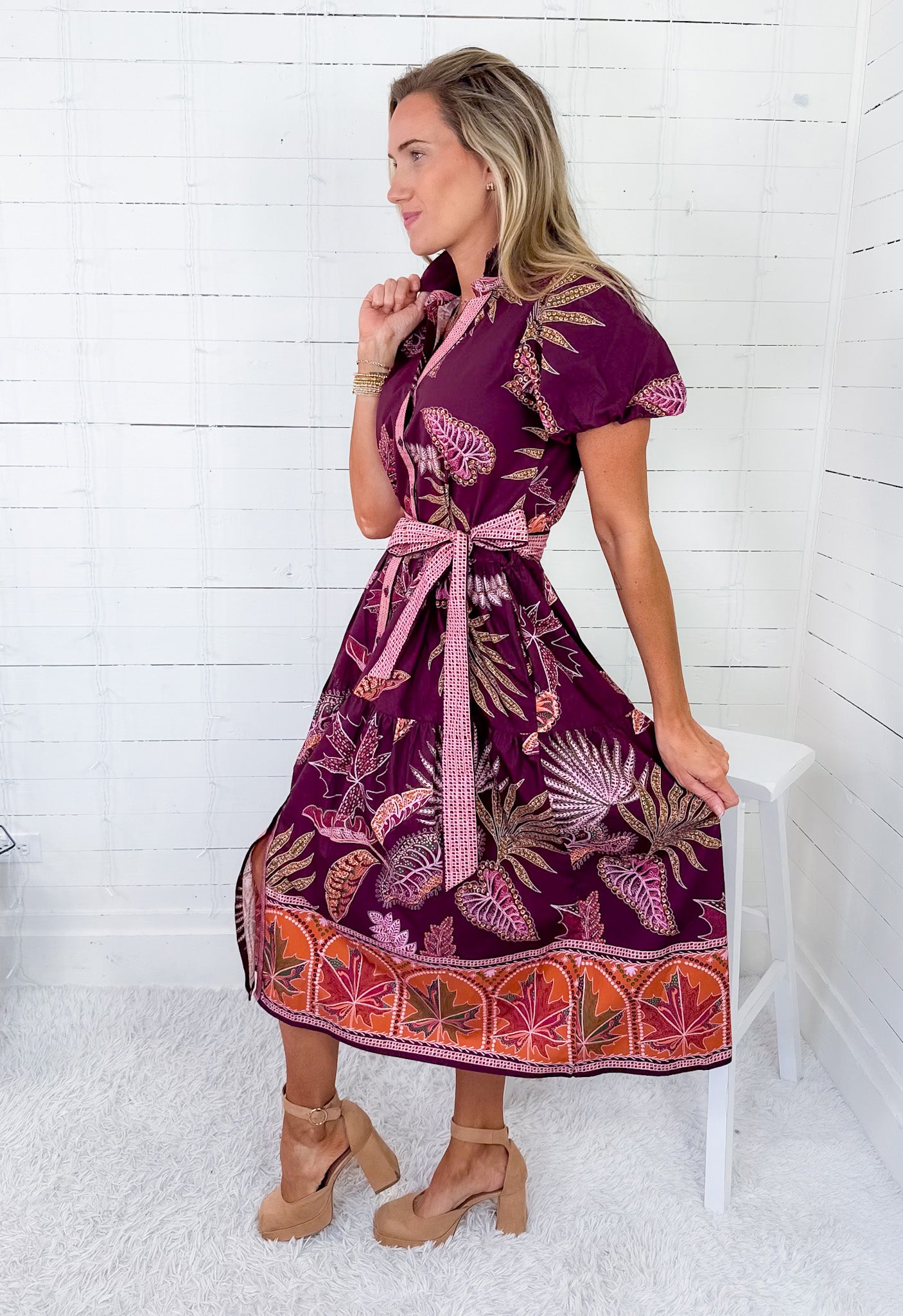 Woman wearing a patterned dress sitting on a white stool against a white wooden panel background