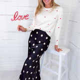 Woman sitting on a stool holding a 'love' sign against a white wooden paneled wall.