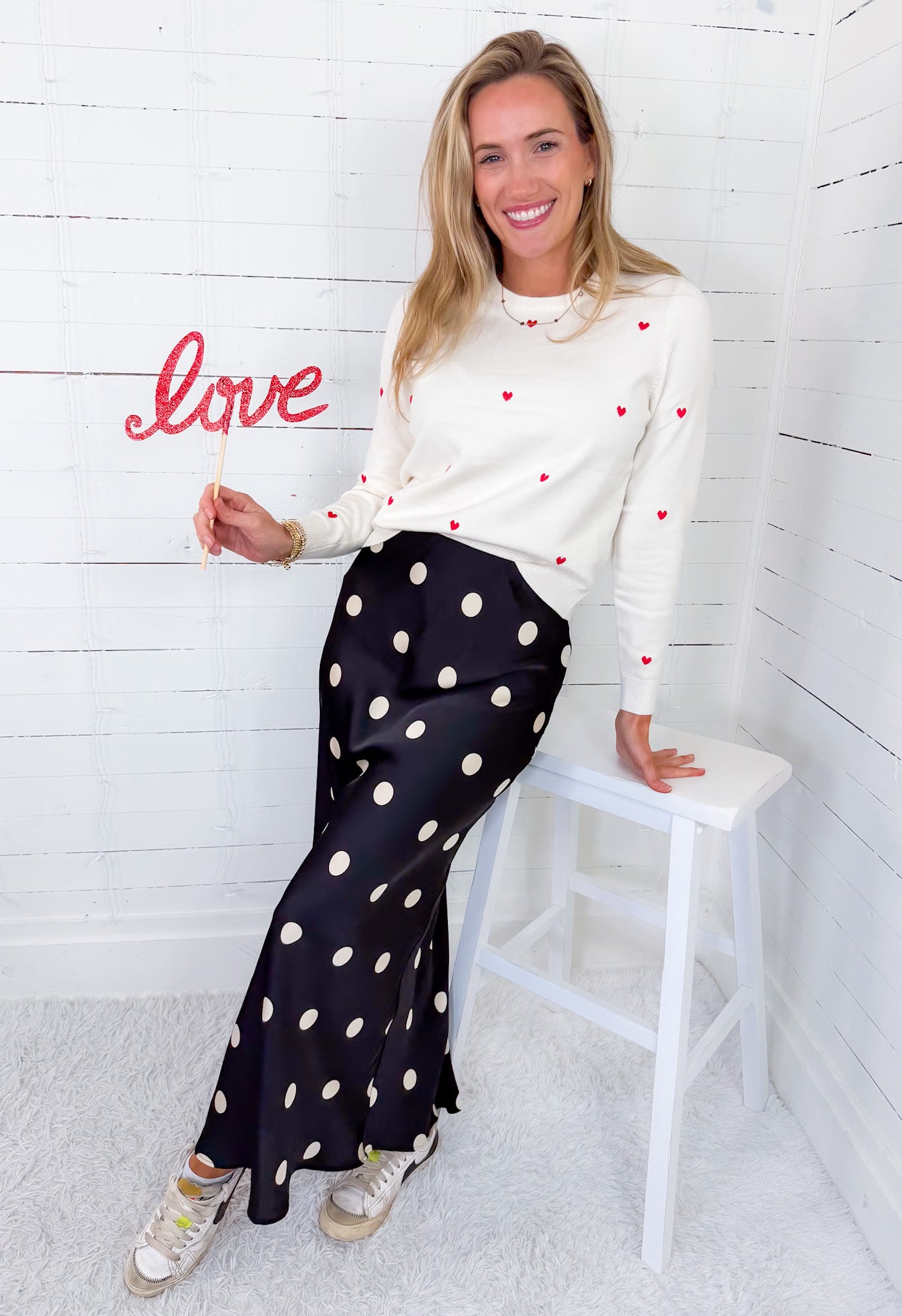 Woman sitting on a stool holding a 'love' sign against a white wooden paneled wall.