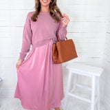 Woman wearing a pink dress with sunglasses and holding a brown bag against a white background