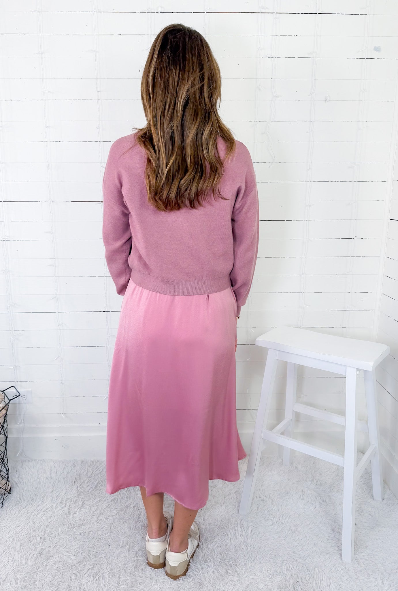 Woman wearing a pink outfit standing against a white wooden paneled wall.