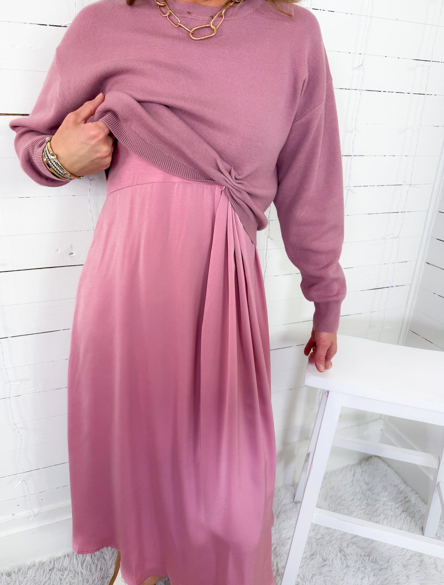 Person wearing a pink dress with long sleeves against a white wooden panel background