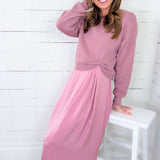 Woman wearing a pink dress sitting on a white stool against a white wooden panel background
