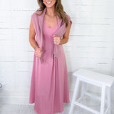 Woman wearing a pink dress with a matching cardigan against a white wooden panel background