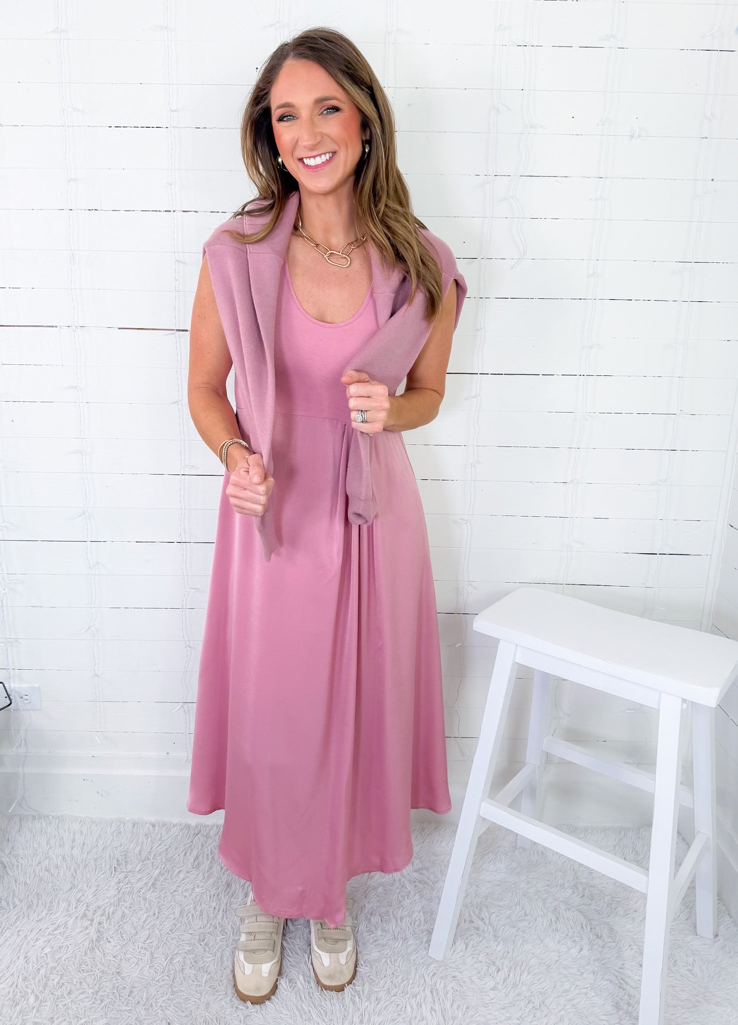 Woman wearing a pink dress with a matching cardigan against a white wooden panel background