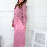 Woman wearing a pink dress standing against a white wooden panel background