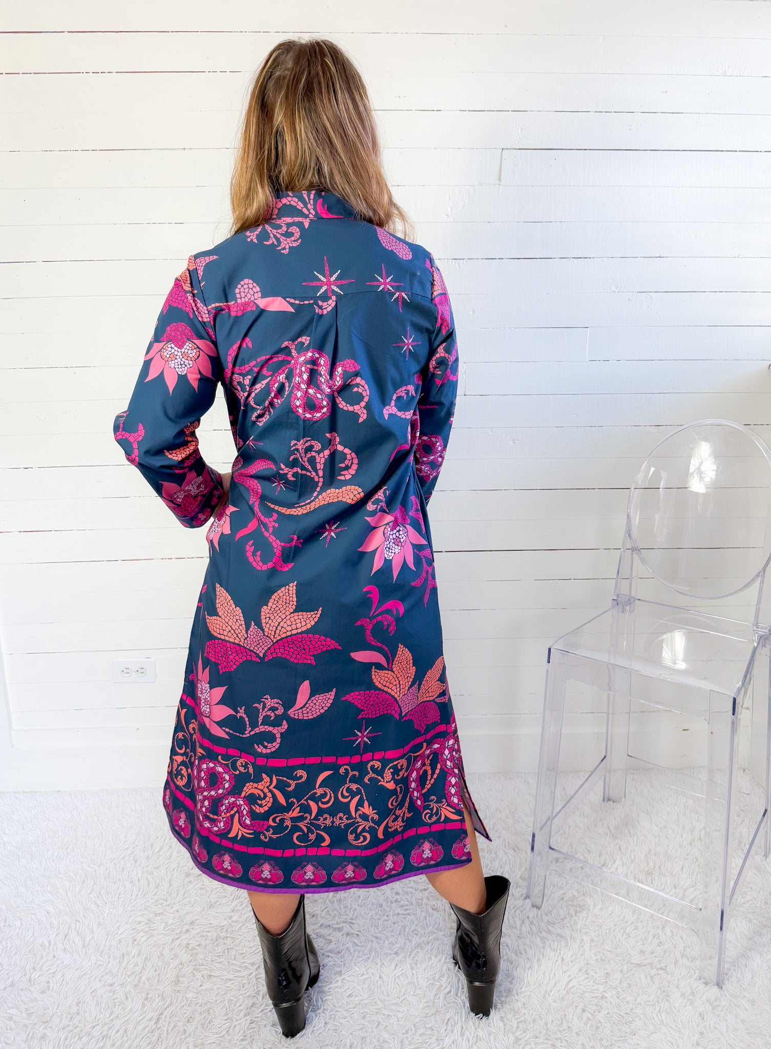 Woman wearing a long, floral-patterned dress with a blue base color against a white wooden panel background.