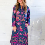 Woman wearing a blue and pink floral dress with black boots in front of a white wooden panel wall.