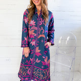 Woman wearing a blue and pink floral dress with black boots in front of a white wooden panel wall.