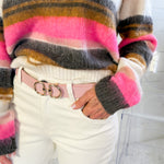 Person wearing a colorful striped sweater and white pants with a pink belt.