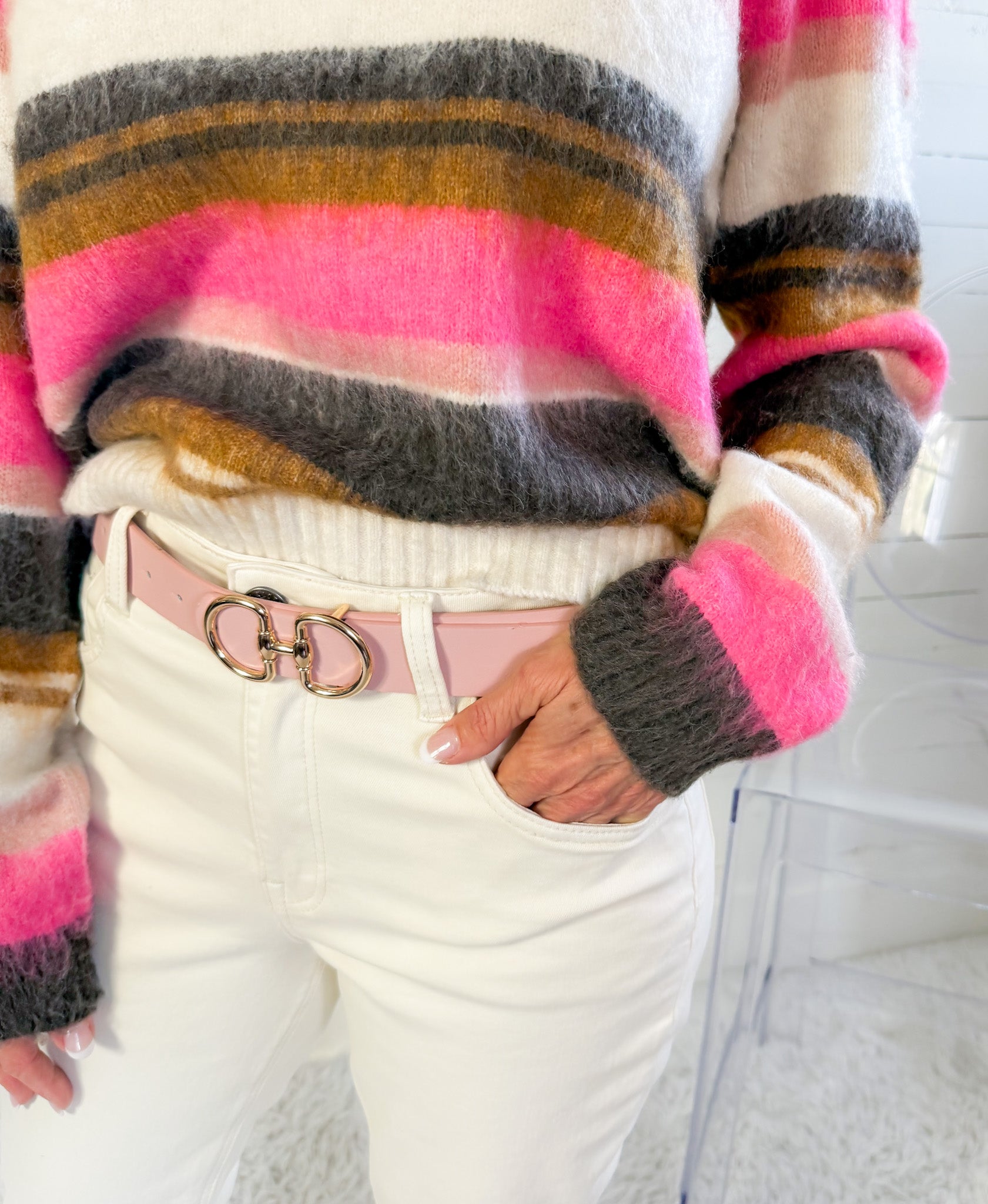 Person wearing a colorful striped sweater and white pants with a pink belt.