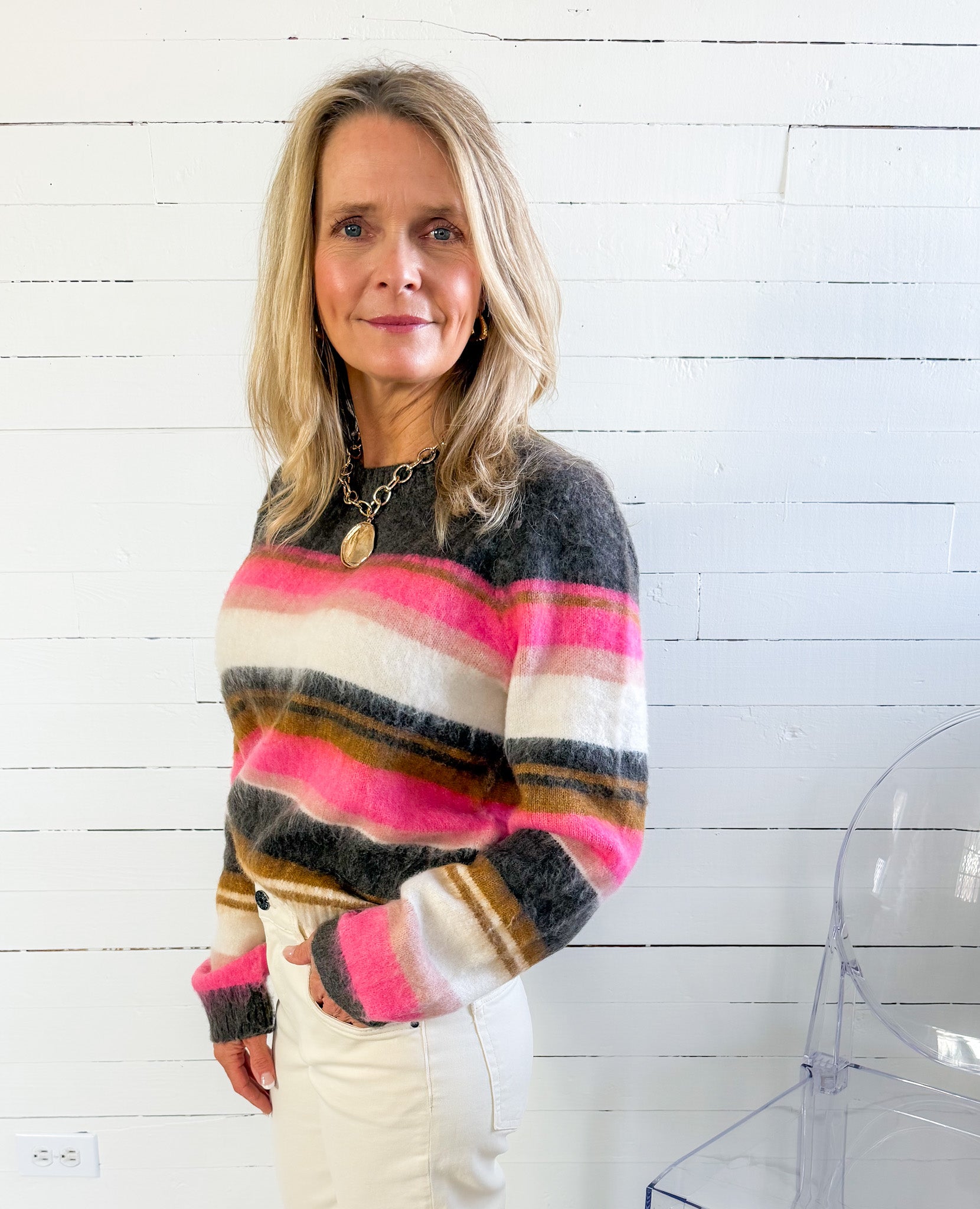 Woman wearing a colorful striped sweater against a white wooden panel background