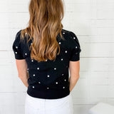 Woman wearing a black sweater with white polka dots against a white wooden panel background