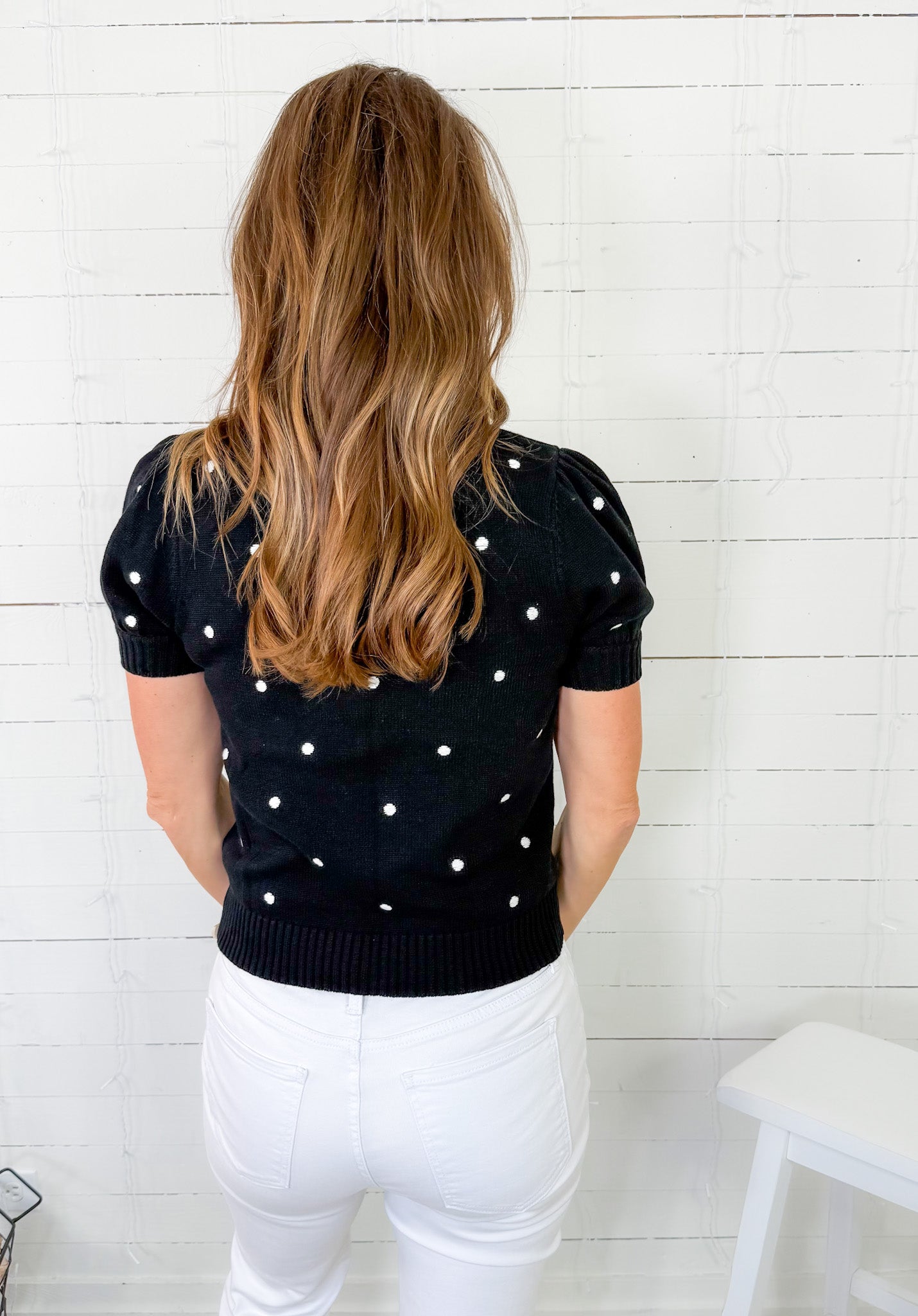 Woman wearing a black sweater with white polka dots against a white wooden panel background