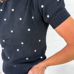 Black sweater with white polka dots worn by a person against a white background