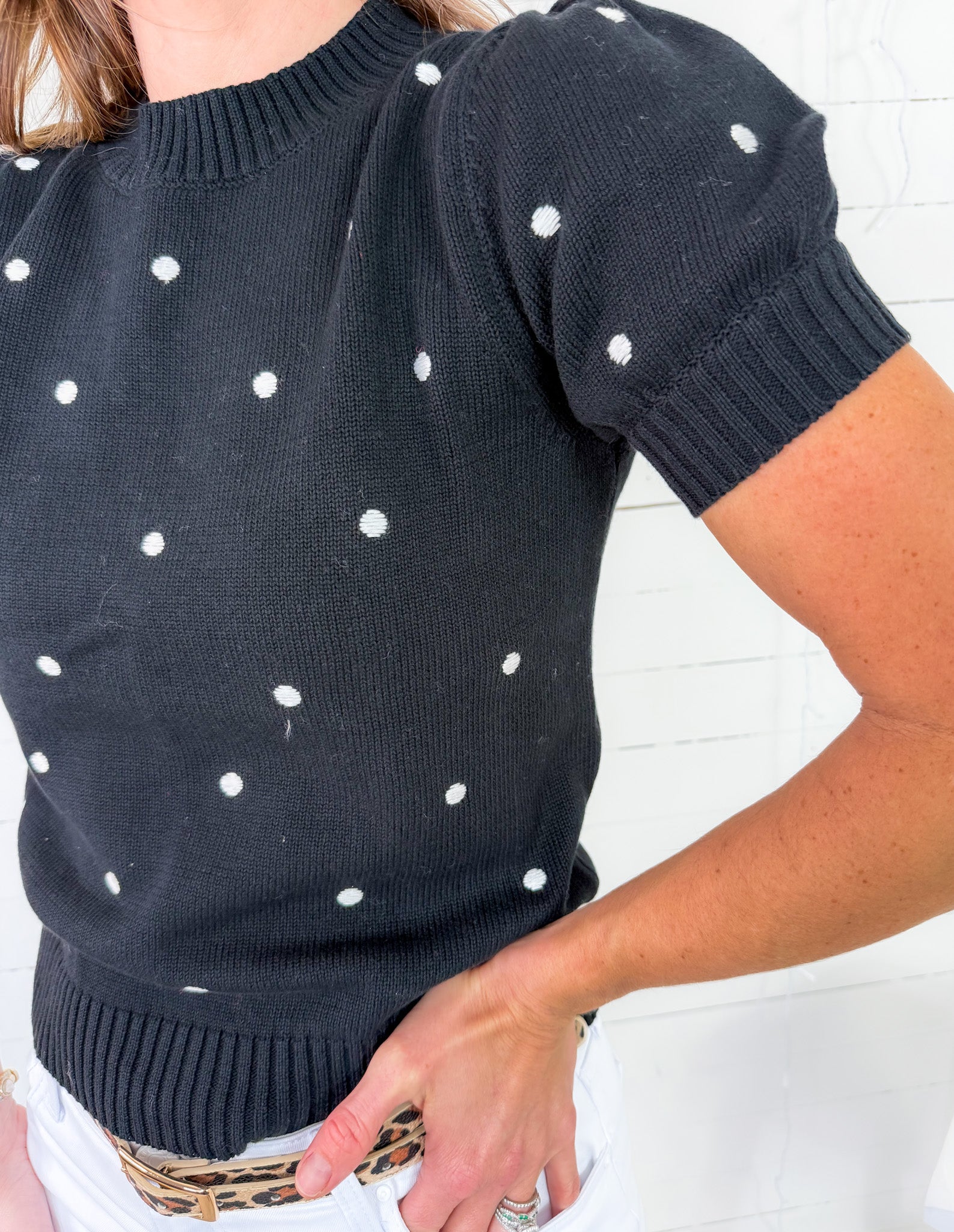 Black sweater with white polka dots worn by a person against a white background