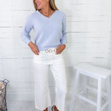 Woman wearing a light blue sweater and white pants in a room with a white wooden floor and a white stool.