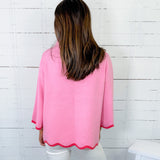 Person wearing a pink blouse with scalloped edges against a white wooden panel background
