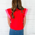 Person wearing a red top with pink sleeves against a white wooden wall.