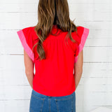 Person wearing a red top with pink sleeves against a white wooden wall.