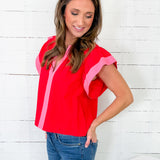 Woman wearing a red top with pink accents against a white wooden panel background