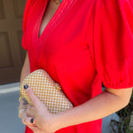 Person wearing a red dress holding a gold clutch against a neutral background