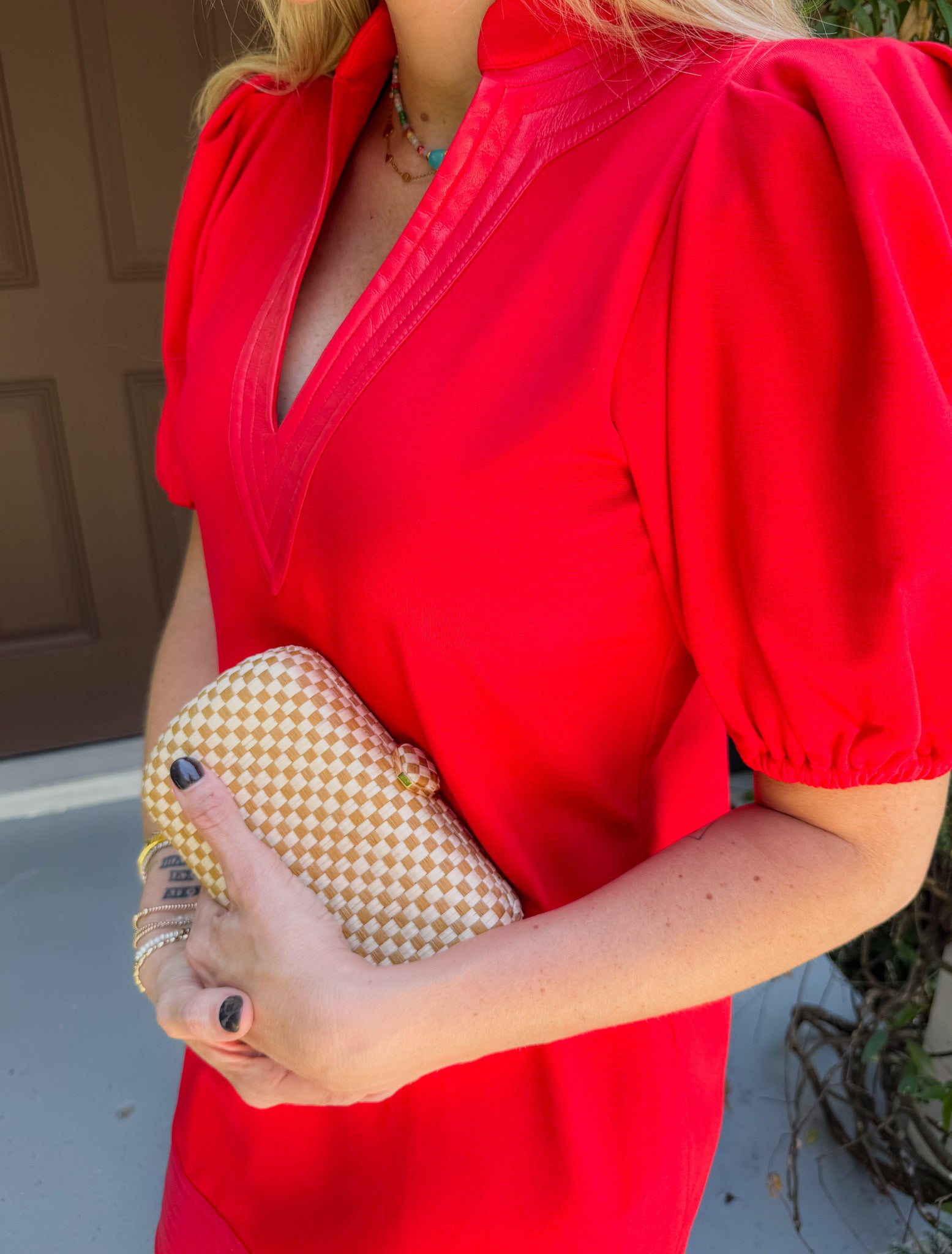 Person wearing a red dress holding a gold clutch against a neutral background
