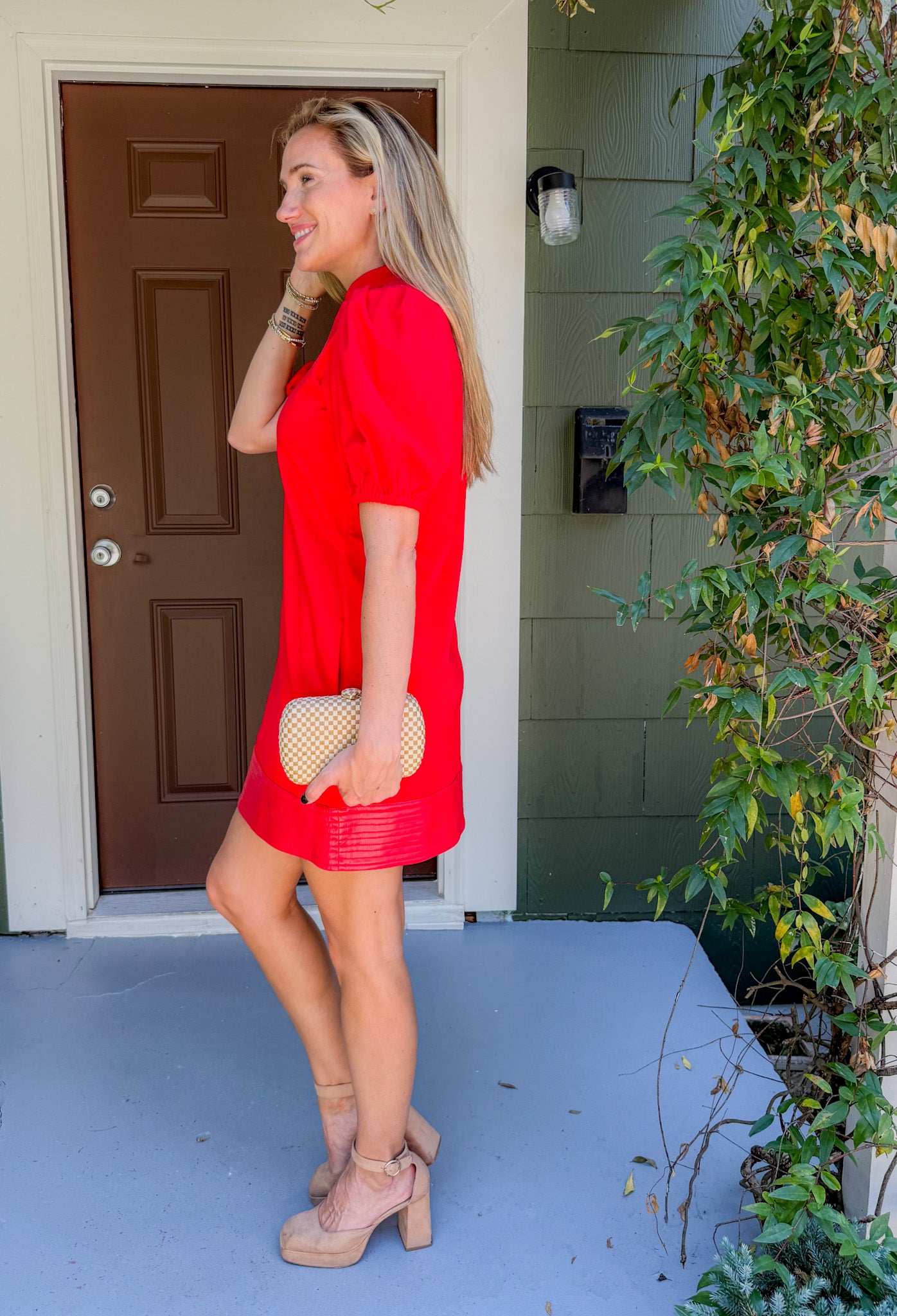 Woman in a red dress standing on a porch with a plant and door in the background
