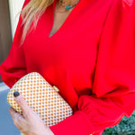 Person wearing a red blouse holding a gold clutch with a blurred background