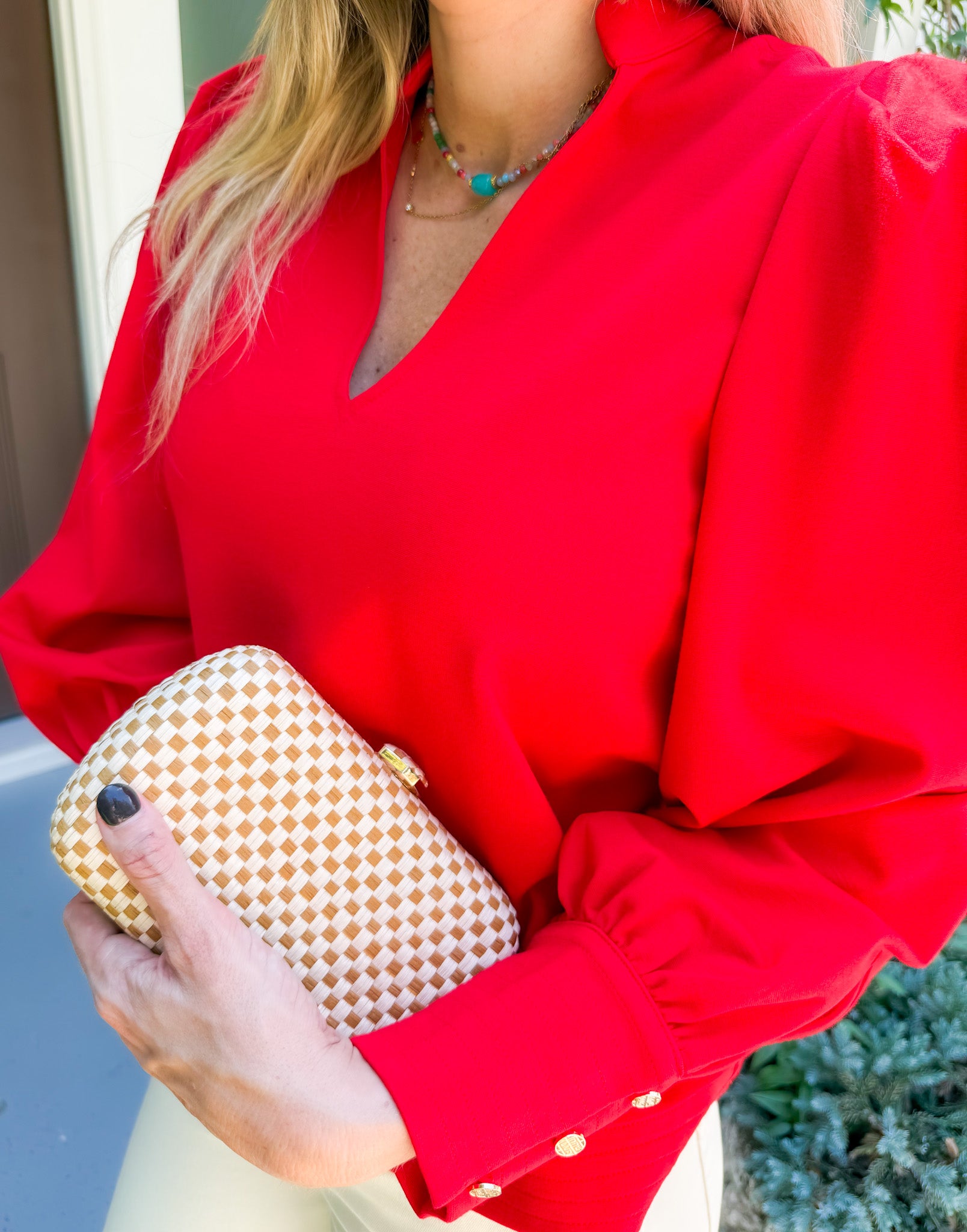 Person wearing a red blouse holding a gold clutch with a blurred background