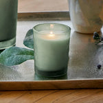 Green candle in a glass holder on a wooden surface with decorative elements.