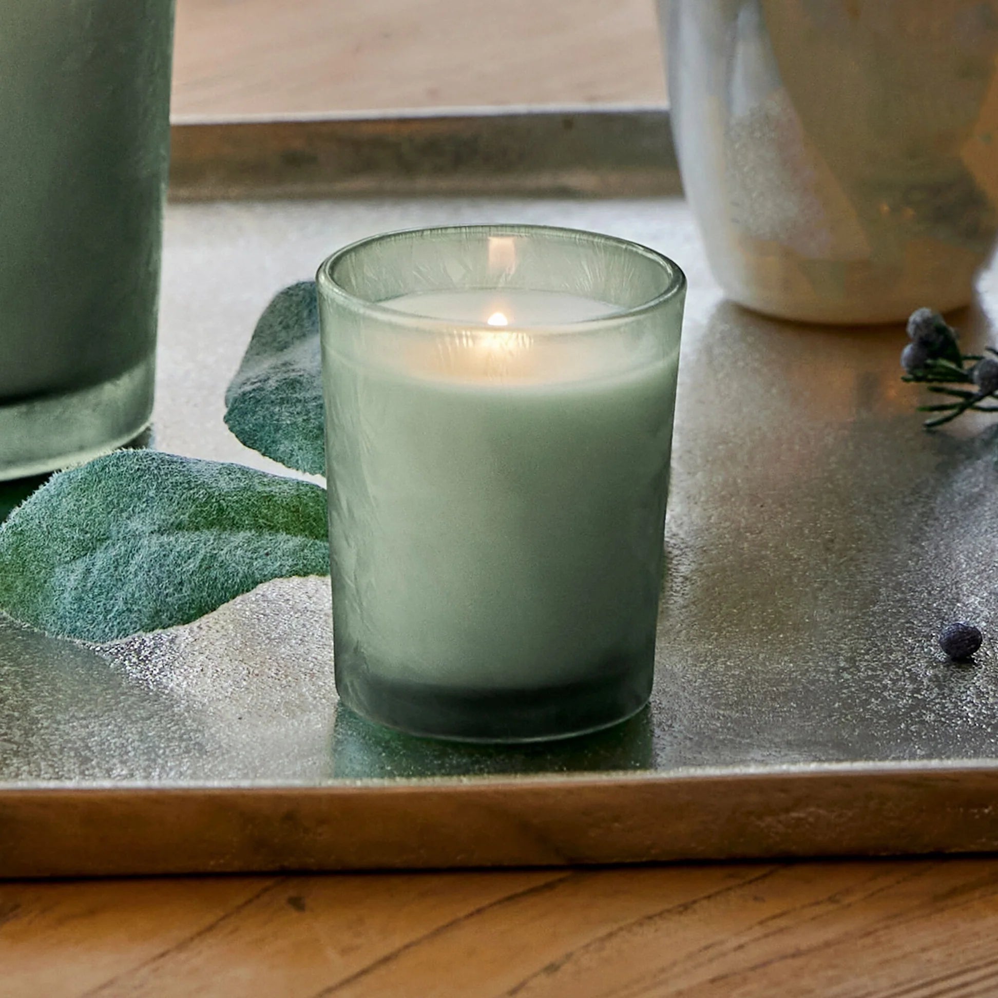 Green candle in a glass holder on a wooden surface with decorative elements.