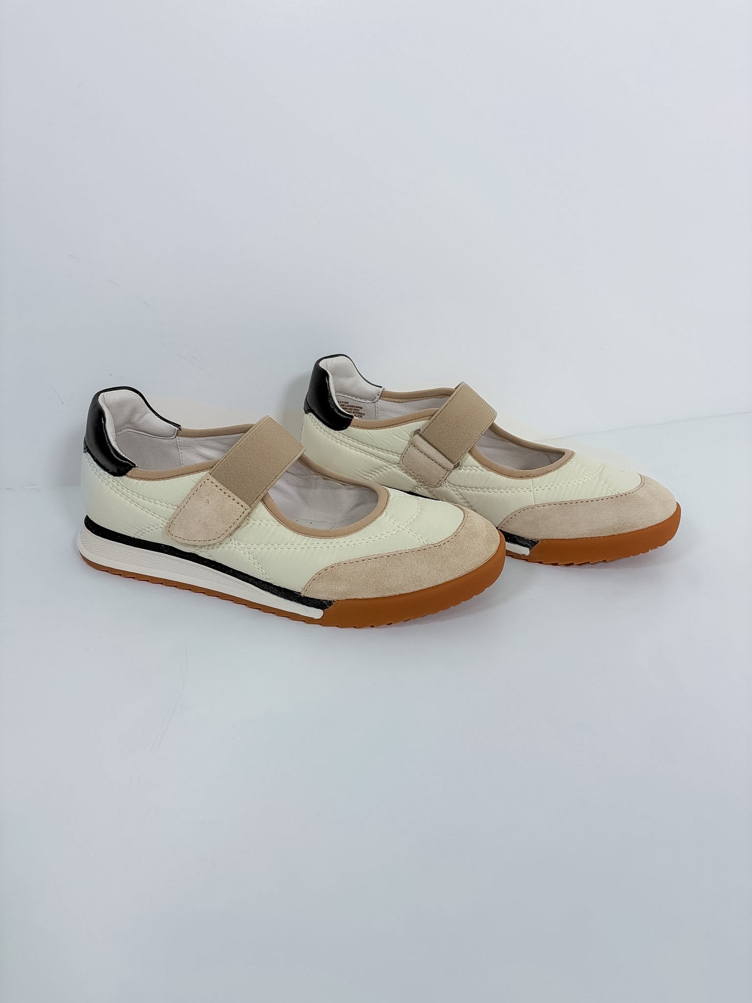 A pair of women's casual Mary Jane-style shoes in cream and beige, featuring a hook-and-loop strap, black heel accents, and brown soles, photographed on a light gray studio background.
