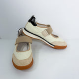 A pair of women's Mary Jane style sneakers in cream and beige suede, featuring a beige hook-and-loop strap, a black heel accent, and a brown sole.