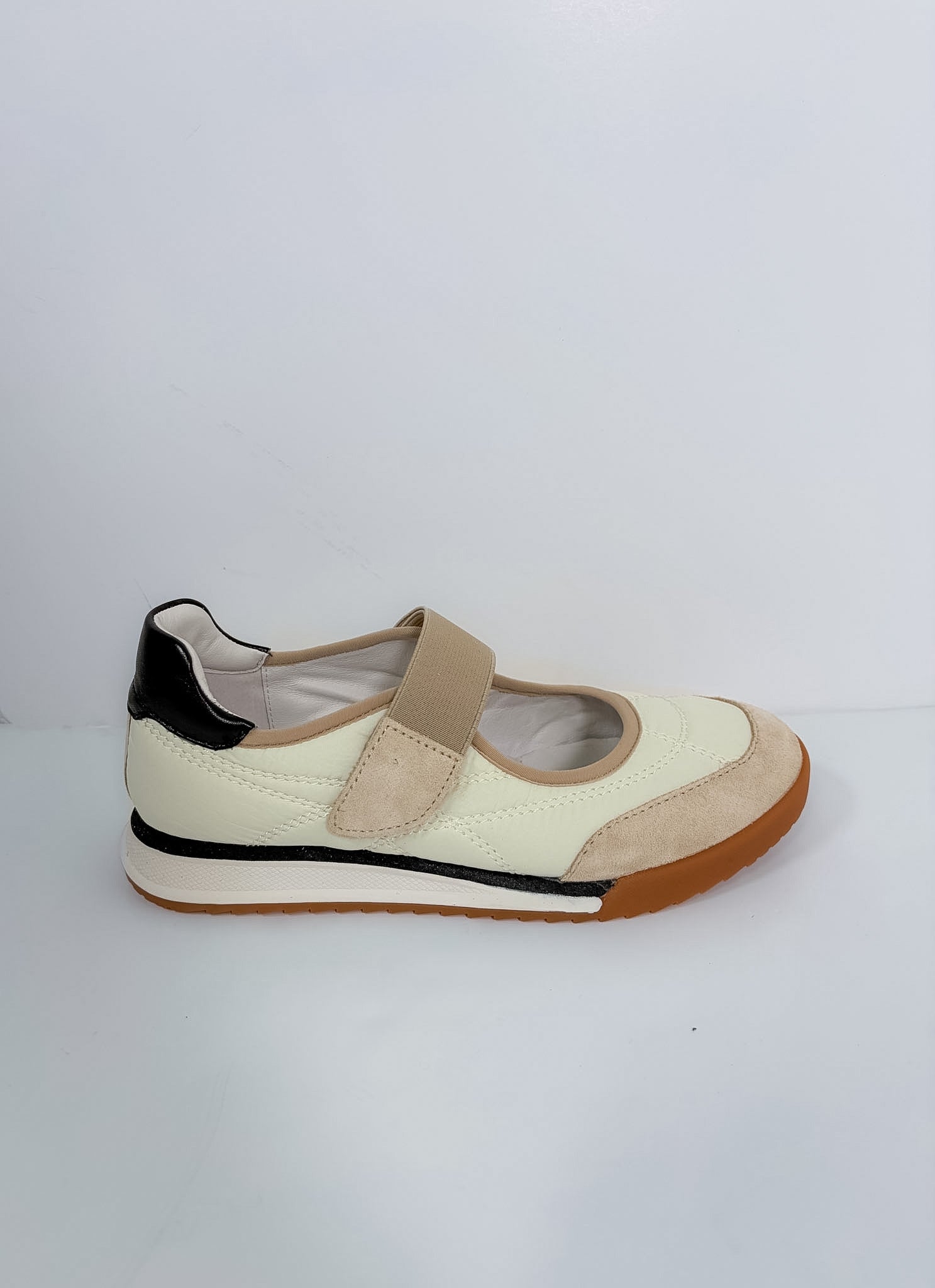 A single women's casual shoe shown in profile against a plain light gray background. The shoe features an off-white leather upper with beige suede panels, a beige hook-and-loop strap, a black heel tab, and a brown gum outsole.