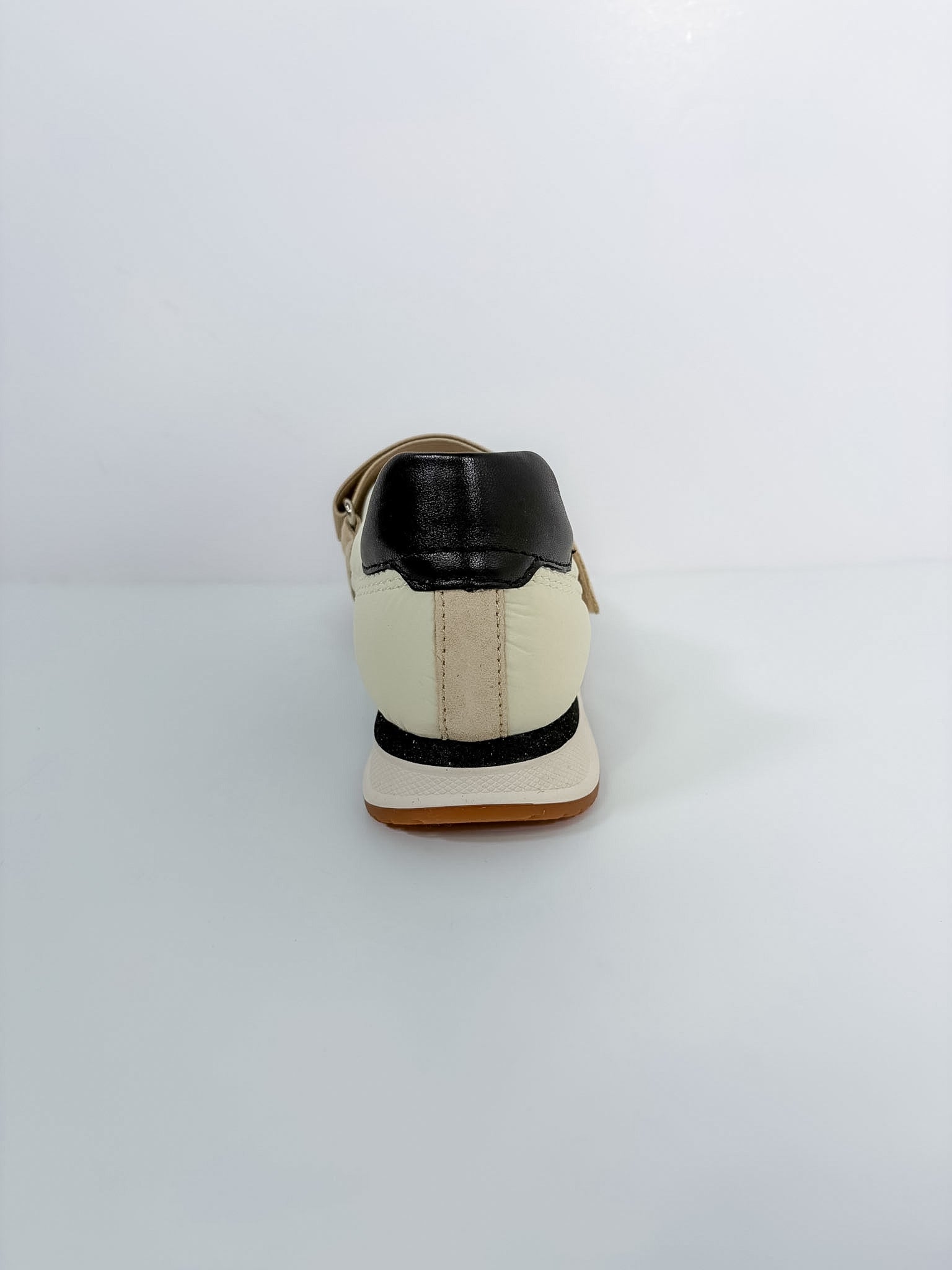 A single low-top shoe shown from the back, featuring an off-white leather upper with a black leather heel tab, a black horizontal stripe, and a tan sole.