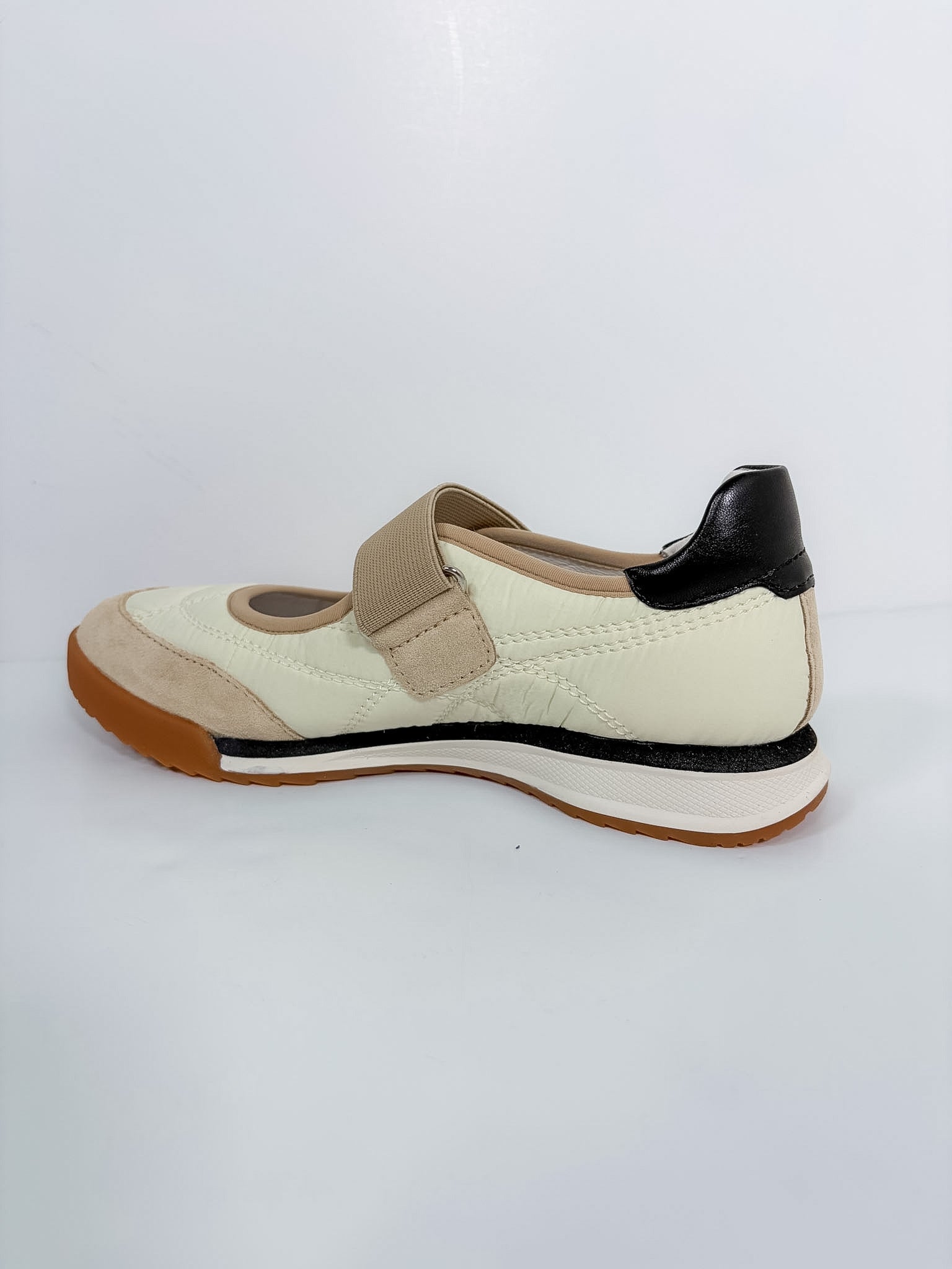 A women's Mary Jane style shoe in cream, beige, and black, featuring a hook-and-loop strap closure and a brown outsole, shown from a side profile on a white background.