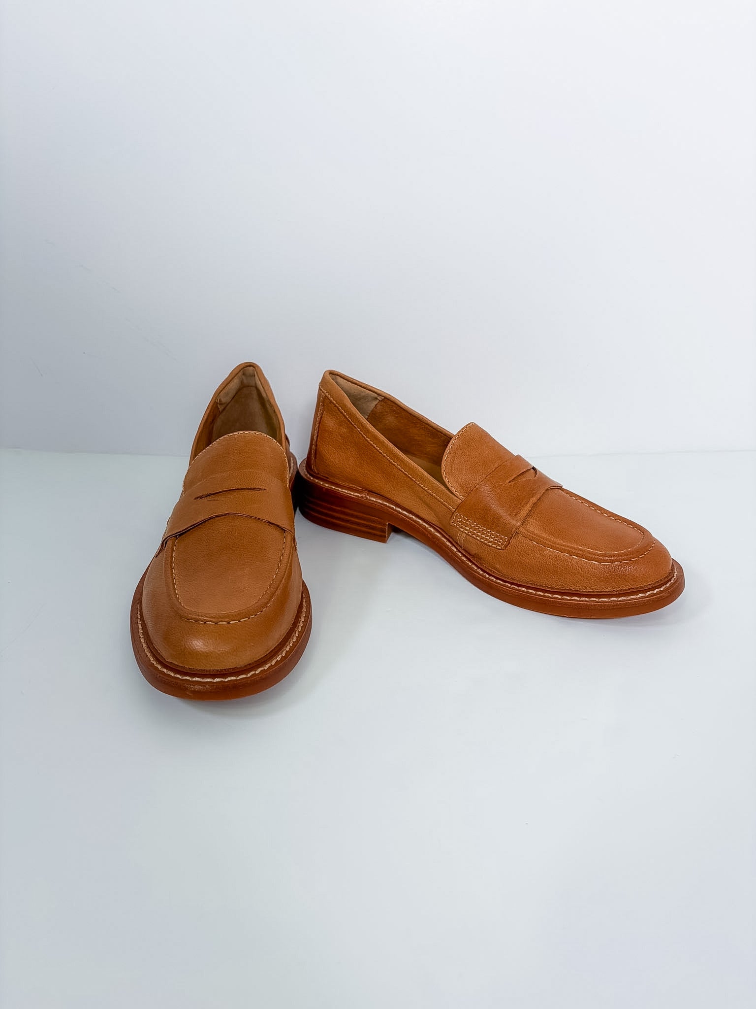 A pair of tan leather penny loafers with low stacked heels, displayed on a clean white studio background.