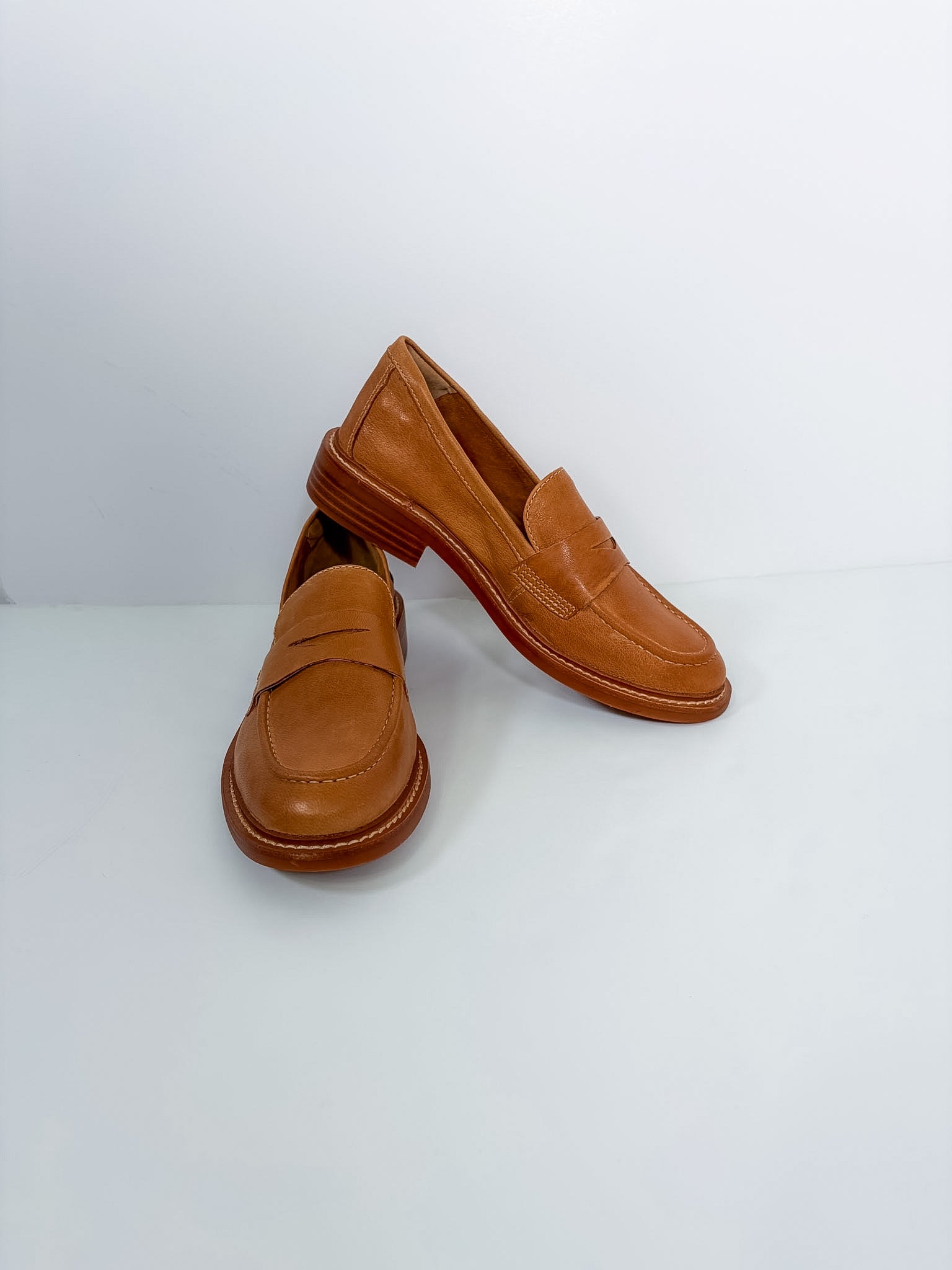 A pair of tan leather penny loafers with brown soles, displayed on a clean white studio background.