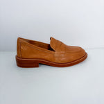 A single tan leather penny loafer shoe with a low stacked heel, shown in profile against a light gray background.