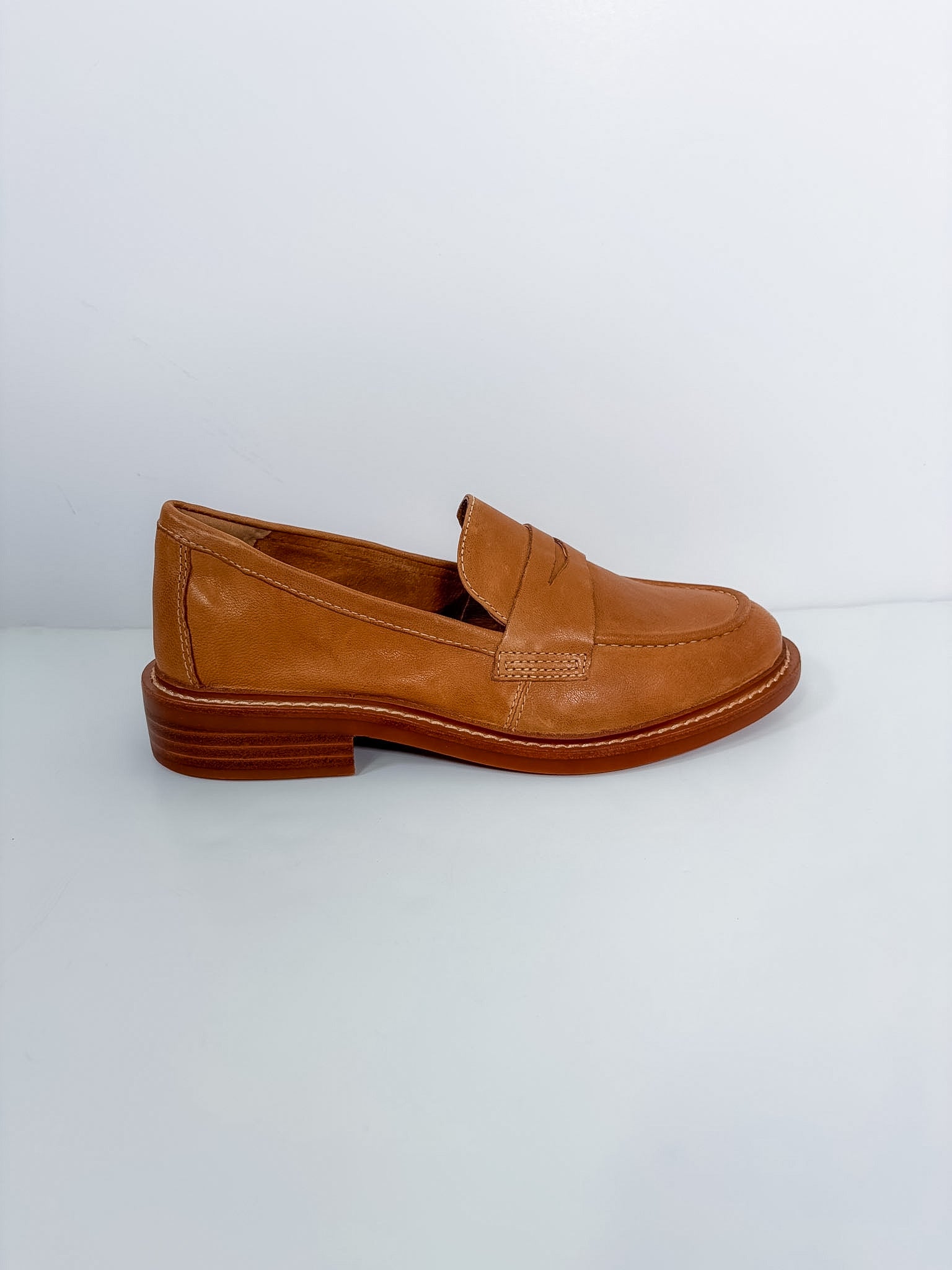 A single tan leather penny loafer shoe with a low stacked heel, shown in profile against a light gray background.